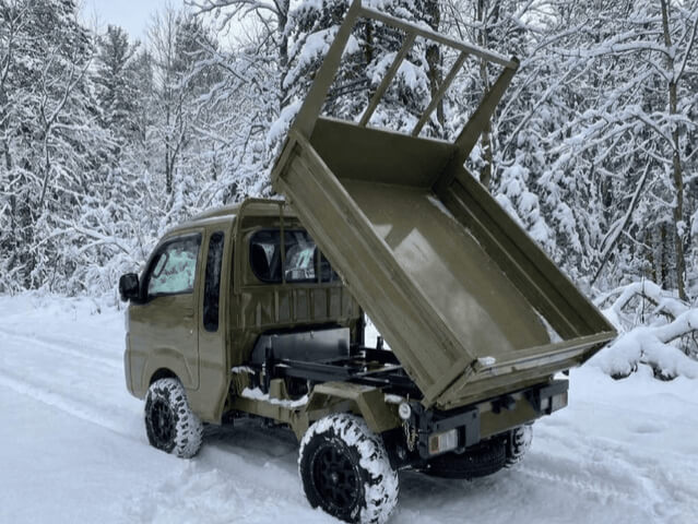 Daihatsu Hijet Jumbo model with Scissor Dump 4x4 Japanese mini truck in green seen from the left rear with the bed showing dumping action in snow.