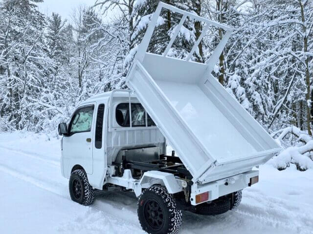 Daihatsu Hijet Jumbo model with Scissor Dump 4x4 Japanese mini truck in white seen from the left rear with the bed showing dumping action in snow.