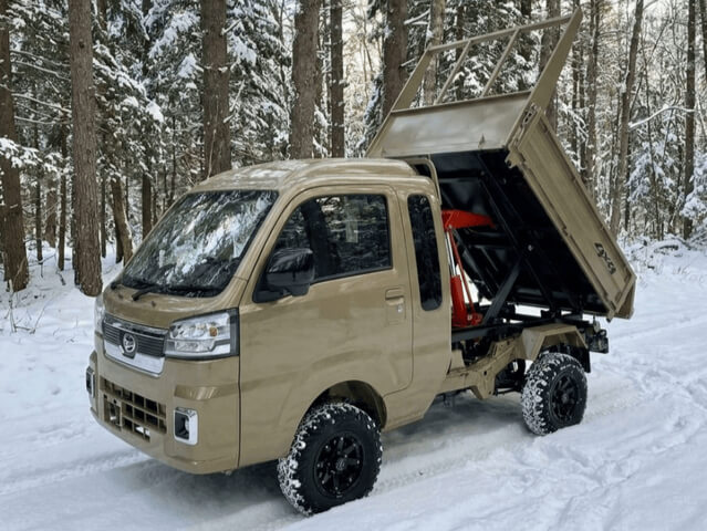 Daihatsu Hijet Jumbo model with Scissor Dump bed 4x4 Japanese mini truck in green seen from the right front with bed showing dumping action in snow.